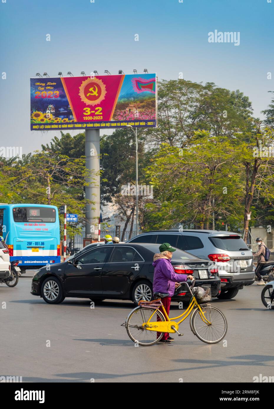 A Vietnamese woman holds her yellow bicycle  under a banner proclaiming the 93rd anniversary of the Vietnam Communist Party in the middle of the road Stock Photo