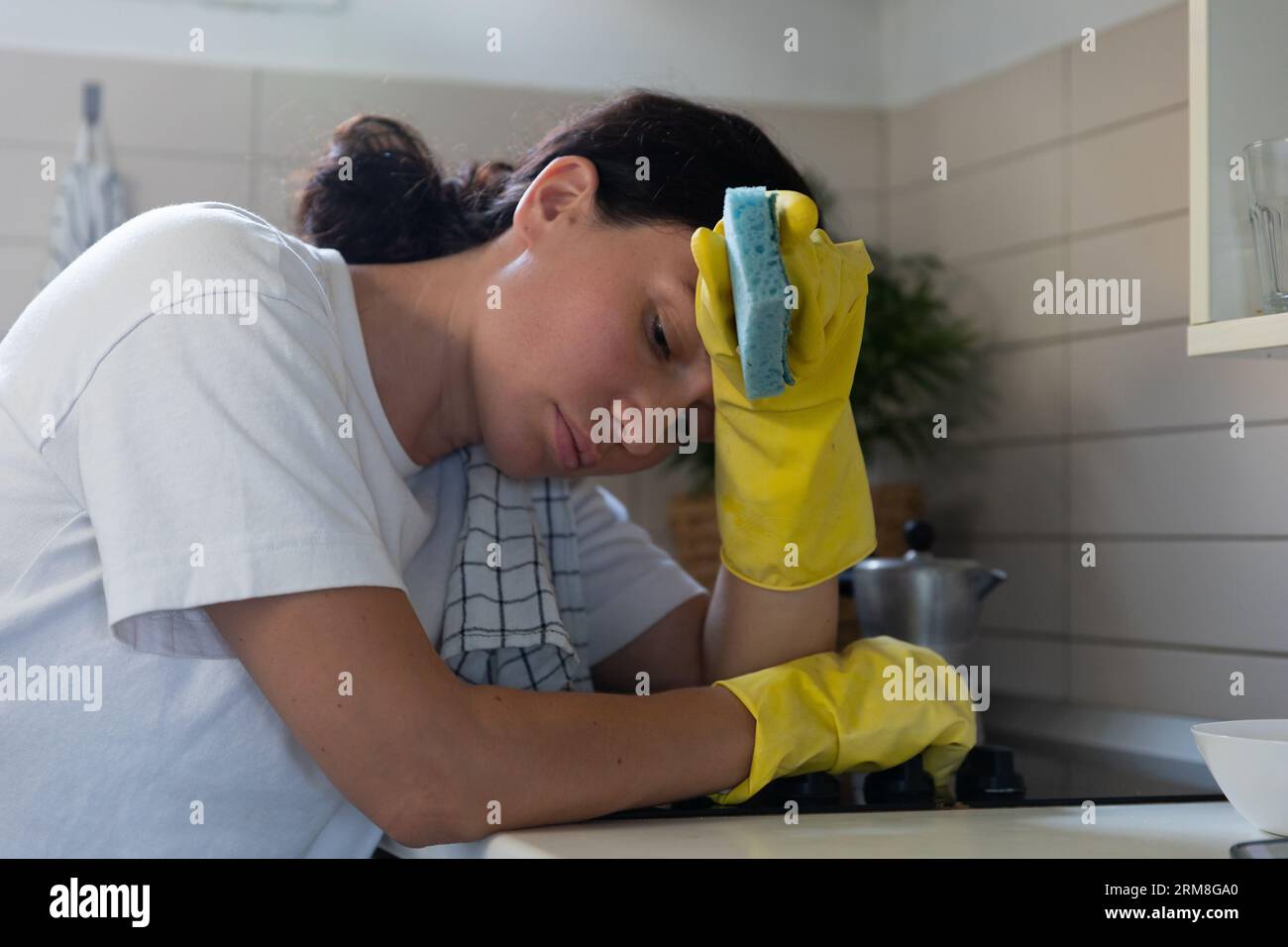 A housewife girl, tired, rubs the stove with gloves. Household routine woman labor Stock Photo