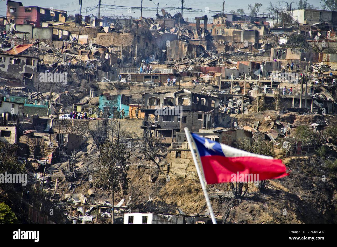 A national flag of Chile waves in front of houses destroyed by a fire in Valparaiso, Chile on April 13, 2014. At least 11 people were killed over the weekend in a massive forest fire that broke out in Chile s port city of Valparaiso, authorities said Sunday. President Michelle Bachelet declared state of emergency in the city and sent the army in to maintain order as thousands of residents were evacuated. (Xinhua/Pablo Ovalle/AGENCIA UNO) CHILE-VALPARAISO-FIRE PUBLICATIONxNOTxINxCHN   a National Flag of Chile Waves in Front of Houses destroyed by a Fire in Valparaiso Chile ON April 13 2014 AT l Stock Photo