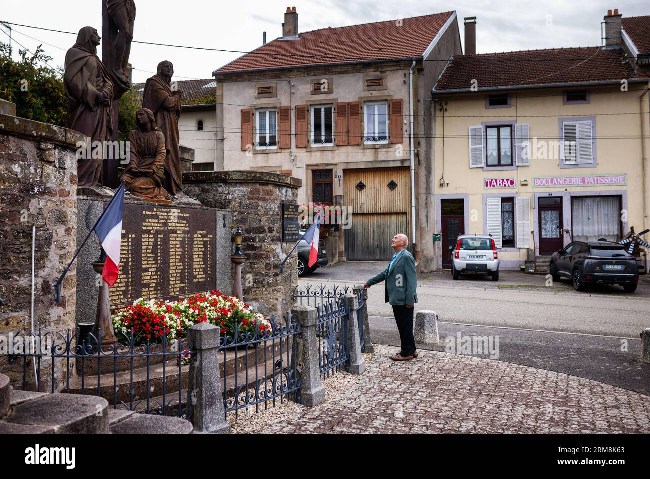 Pexonne, France. 27th Aug, 2023. A man stands in front of a memorial plaque to the victims of the August 27, 1944 raid on Pexonne, which can be seen next to the village's church. In late August 1944, German soldiers invaded the French village of Pexonne and kidnapped dozens of villagers. The action was led by SS Hauptsturmführer Erich Otto Wenger. Now Wenger's grandchildren came to town for the first time to take part in a memorial service for the victims of the crime. Credit: Philipp von Ditfurth/dpa/Alamy Live News Stock Photo