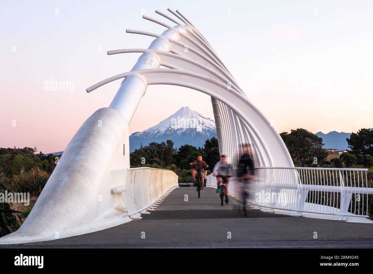 New Plymouth, New Zealand - August 23rd 2017 - Three youths riding their bikes across Te Rewa Rewa Bridge on the Coastal Way with Mt Taranaki Stock Photo