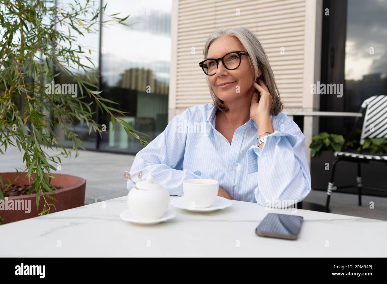 Well Groomed Slender Mature Business Woman With Gray Hair Dressed In A Shirt Sits On The Terrace