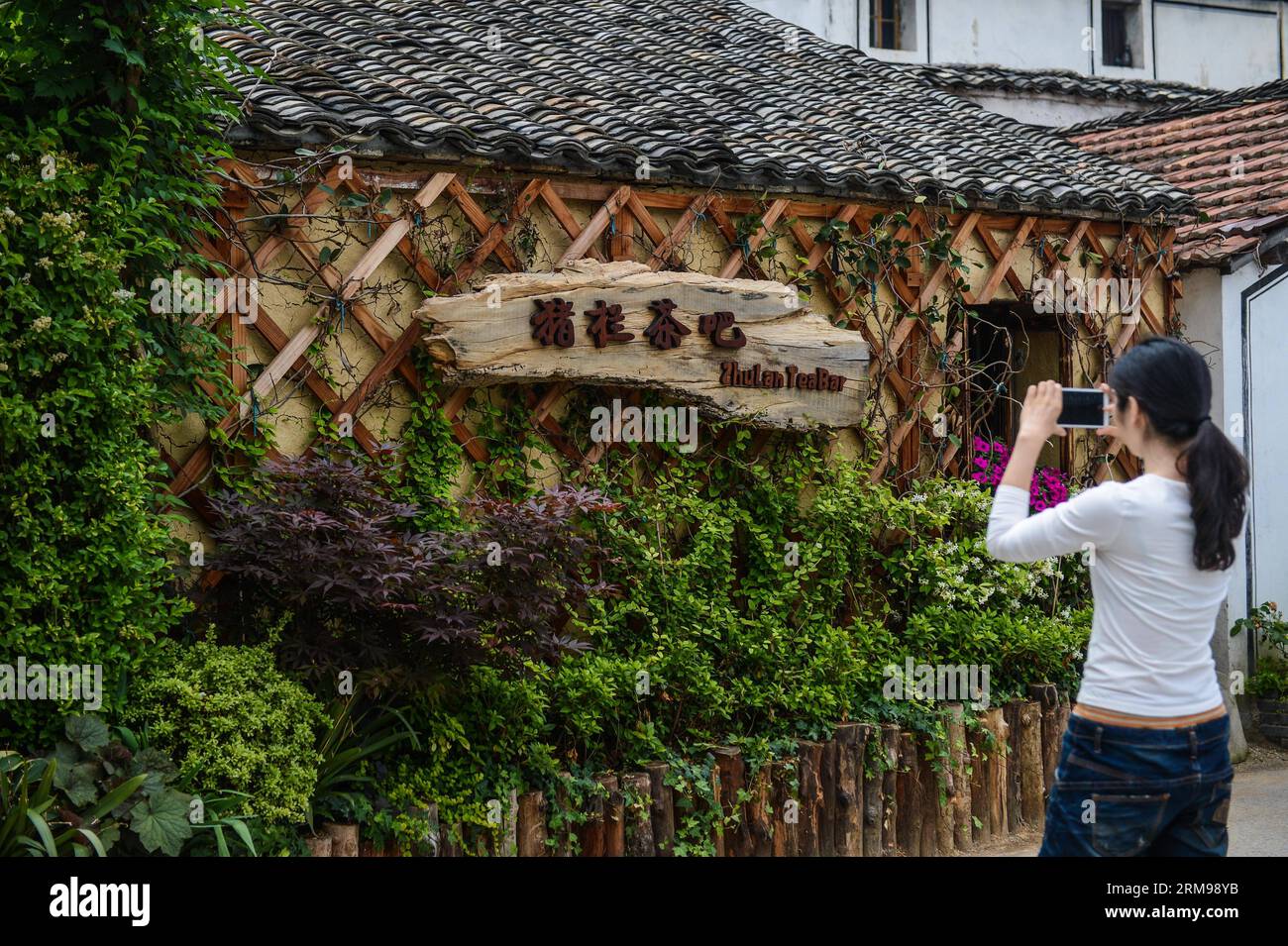 (140513) -- TONGLU, May 13, 2014 (Xinhua) -- A tourist takes photo of the swinery tea bar in Dipu Village of Jiangnan Town in Tonglu County, east China s Zhejiang Province, May 13, 2014. Dipu Village, a national historical and cultural village with nearly a thousand years history, has committed to environment reform, village protection and tourism development for the past few years. The swinery tea bar sets a successful example of the transform. The bar used to be five messy stone houses for pigs keeping. After renovation, it functions as a modern tea bar with traditional appearance, attractin Stock Photo