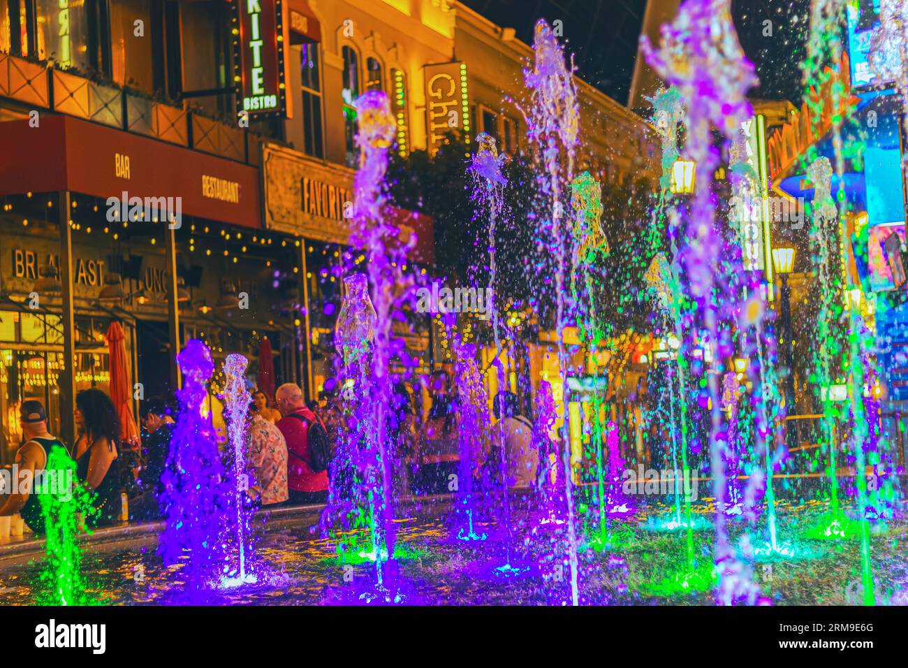 Experience the dazzling spectacle of dancing water jets, captured in a colorful nighttime photograph next to In-N-Out at The LINQ Promenade in Las Veg Stock Photo