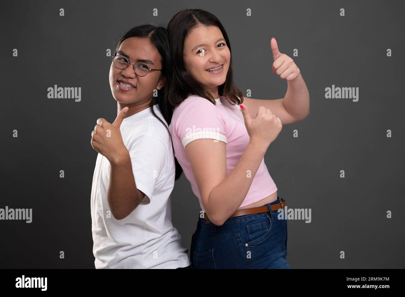Two young people with teeth brackets and thumb up isolated on grey studio background Stock Photo