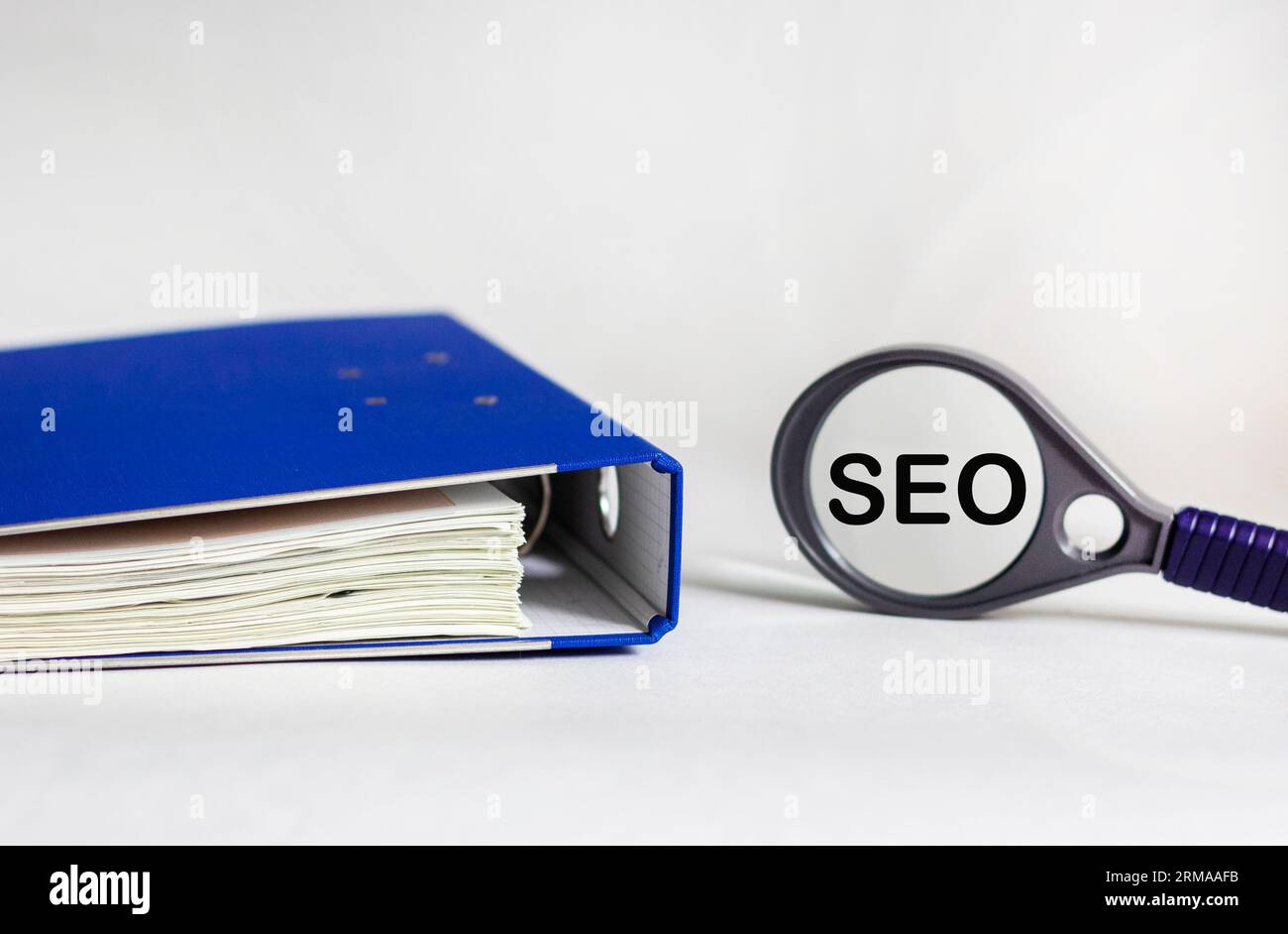 The word SEO written on a magnifying glass and a white background with a blue document folder Stock Photo