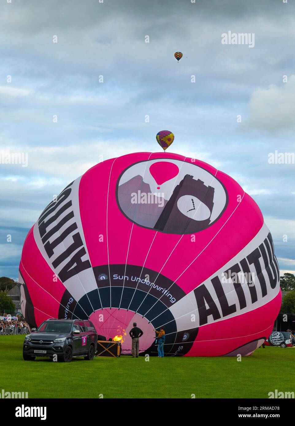 A hot-air balloon being inflated ready for flight while two others fly into the distance during the Strathaven Balloon Festival 2023 in Strathaven, Sc Stock Photo