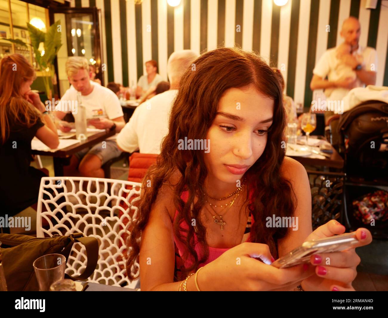 Teenage girl distracted by her mobile phone during dinner in a restaurant. Stock Photo