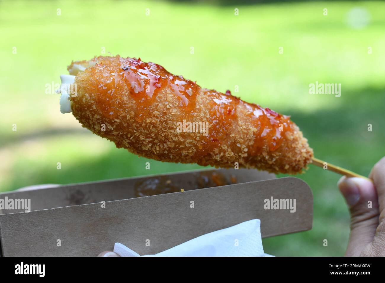 Hand holding Korean style corn dog coated in crispy panko breadcrumbs with hot sauce Stock Photo