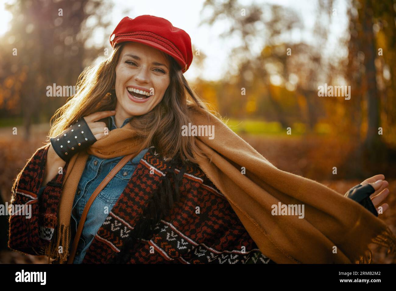 Hello autumn. Portrait of happy elegant 40 years old woman in red hat with scarf and gloves in the city park. Stock Photo