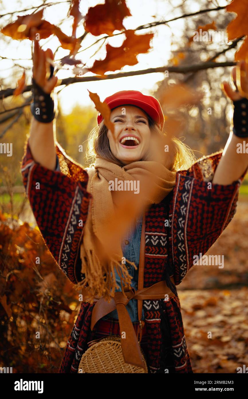 Hello autumn. smiling young woman in red hat with scarf and gloves throwing autumn leafs in the city park. Stock Photo