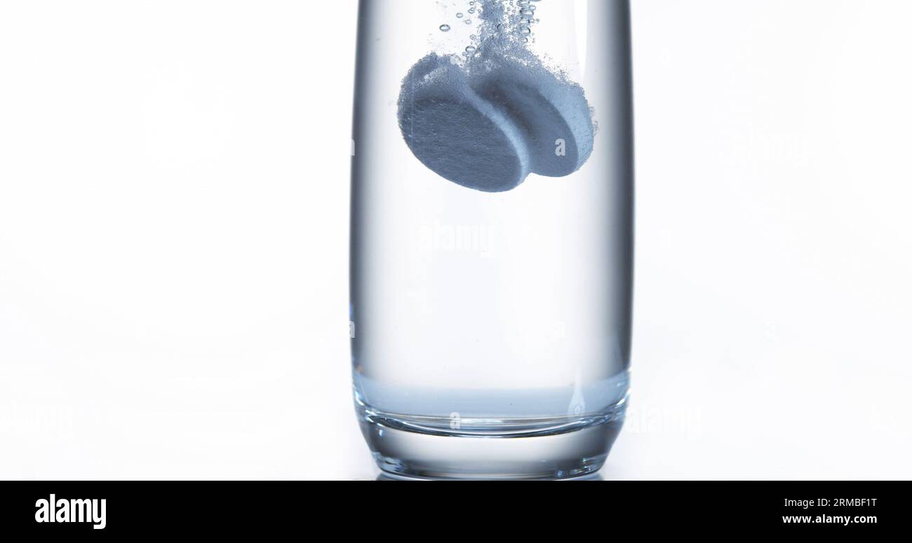 Tablets Falling and Dissolving into a Glass of Water against White