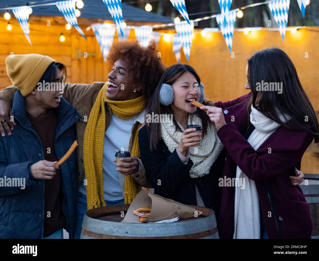 Group of diverse friends in winter eating churros and hot chocolate on the street in Spain Stock Photo