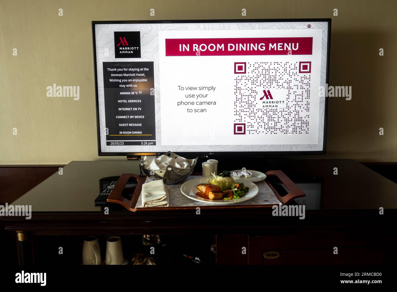 Digital in-room dining menu on a room tv in Marriott Amman Hotel. The room service ordered food tray on a desk in front of TV with menu with QR code Stock Photo