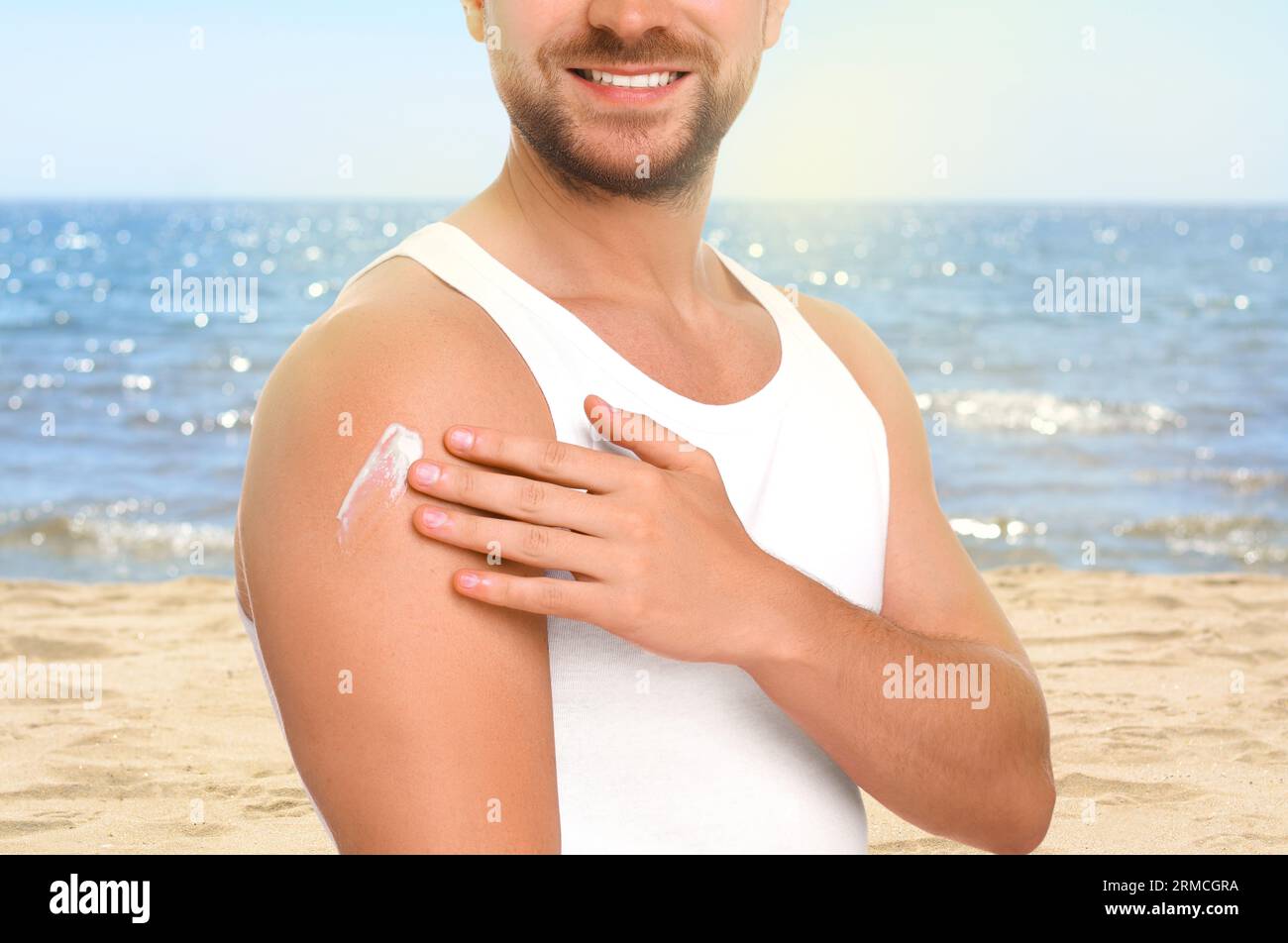 Sun protection. Man applying sunblock onto skin near sea, closeup Stock Photo