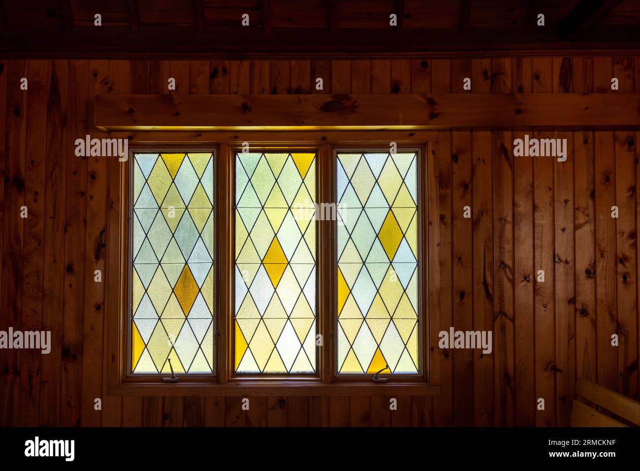 Abstract texture background of a modern window with diamond patterned stain glass, surrounded by a wood paneled wall in a darkened room. Stock Photo