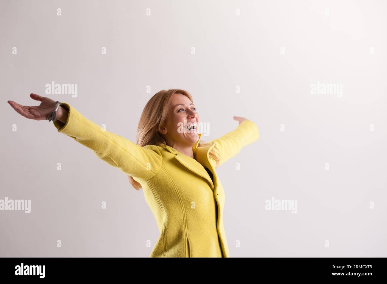Expressing boundless joy with arms outstretched, a blonde woman savors life's essence. She looks up, recognizing her blessings and showing profound gr Stock Photo
