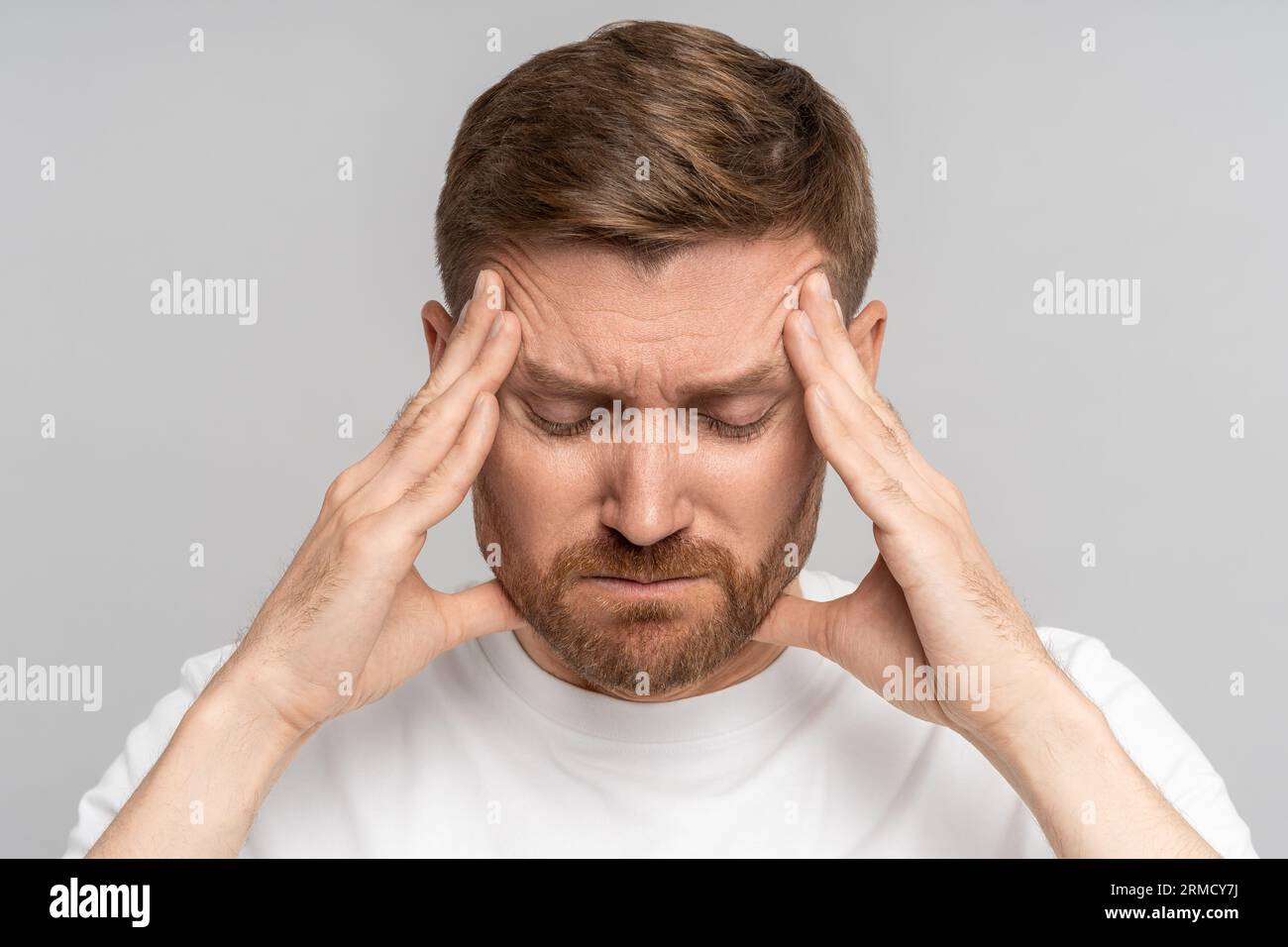 Exhausted man with eyes closed presses fingers to temples from headache