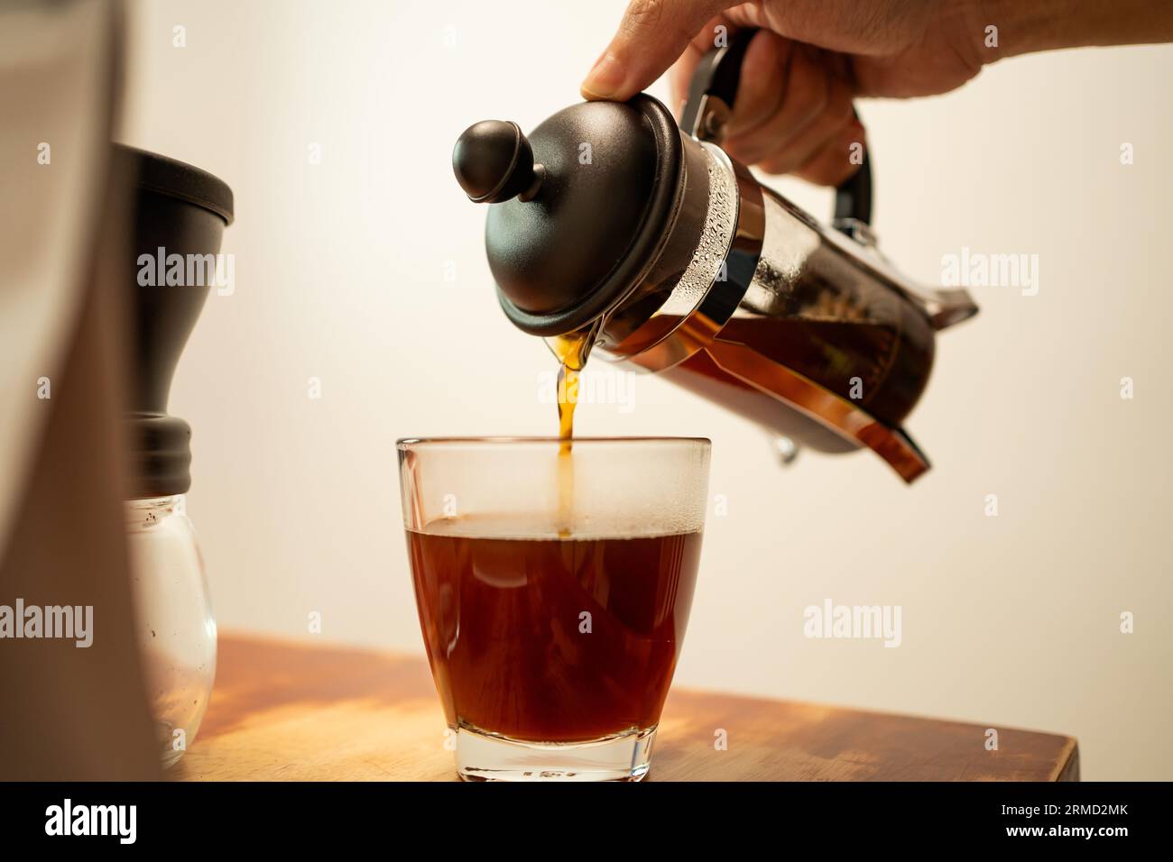 Pouring hot coffee from a french press jug into a drinking glass Stock Photo
