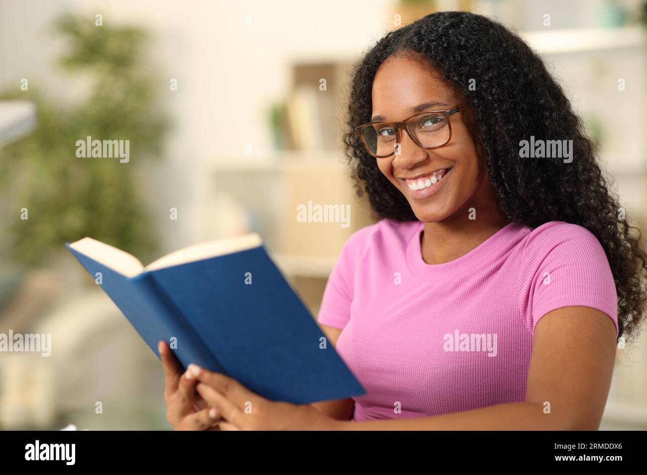 Happy black woman holding paper book with eyeglasses at home Stock Photo