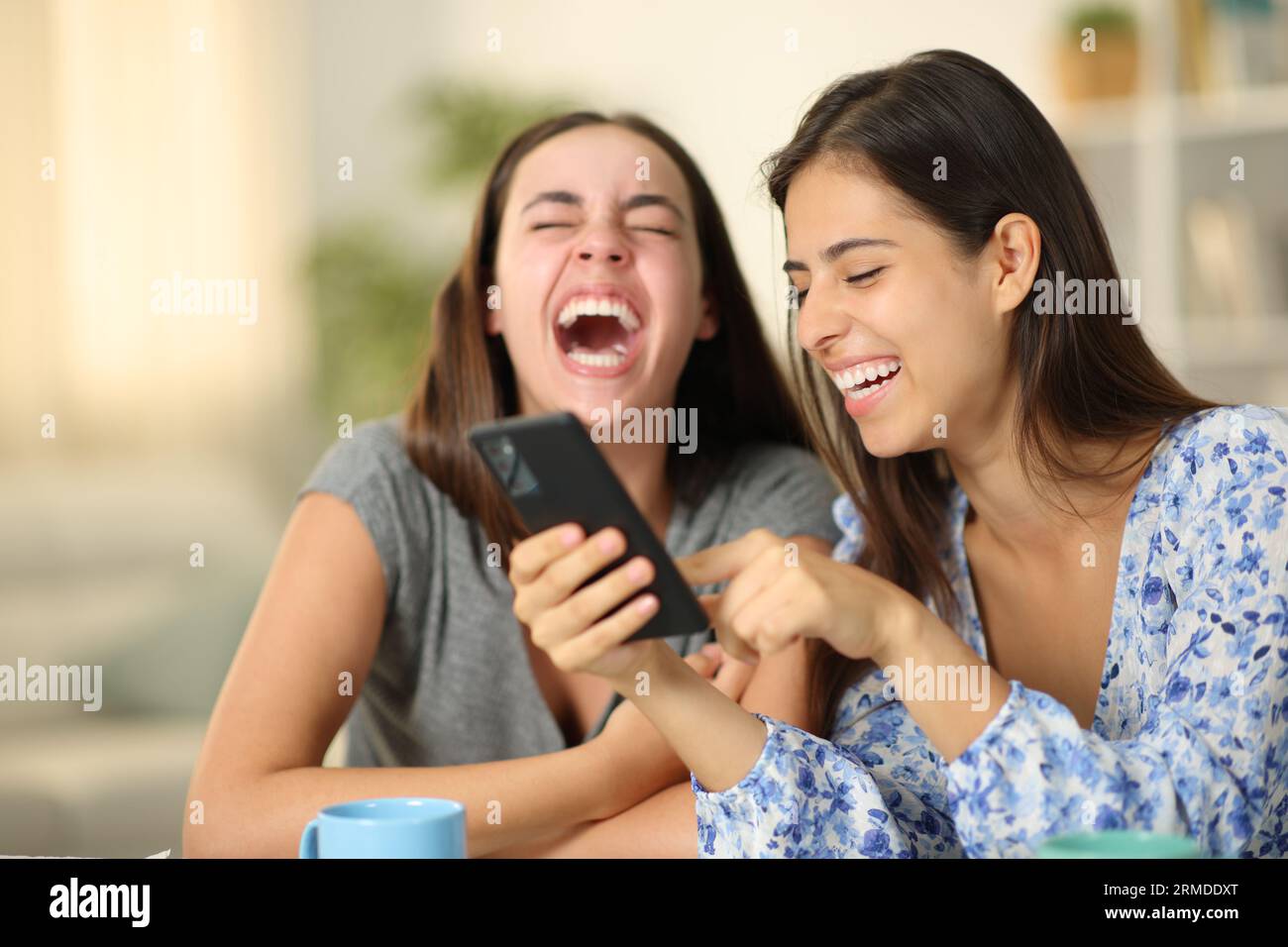 Two happy friends laughing hilarious using phone together at home Stock Photo