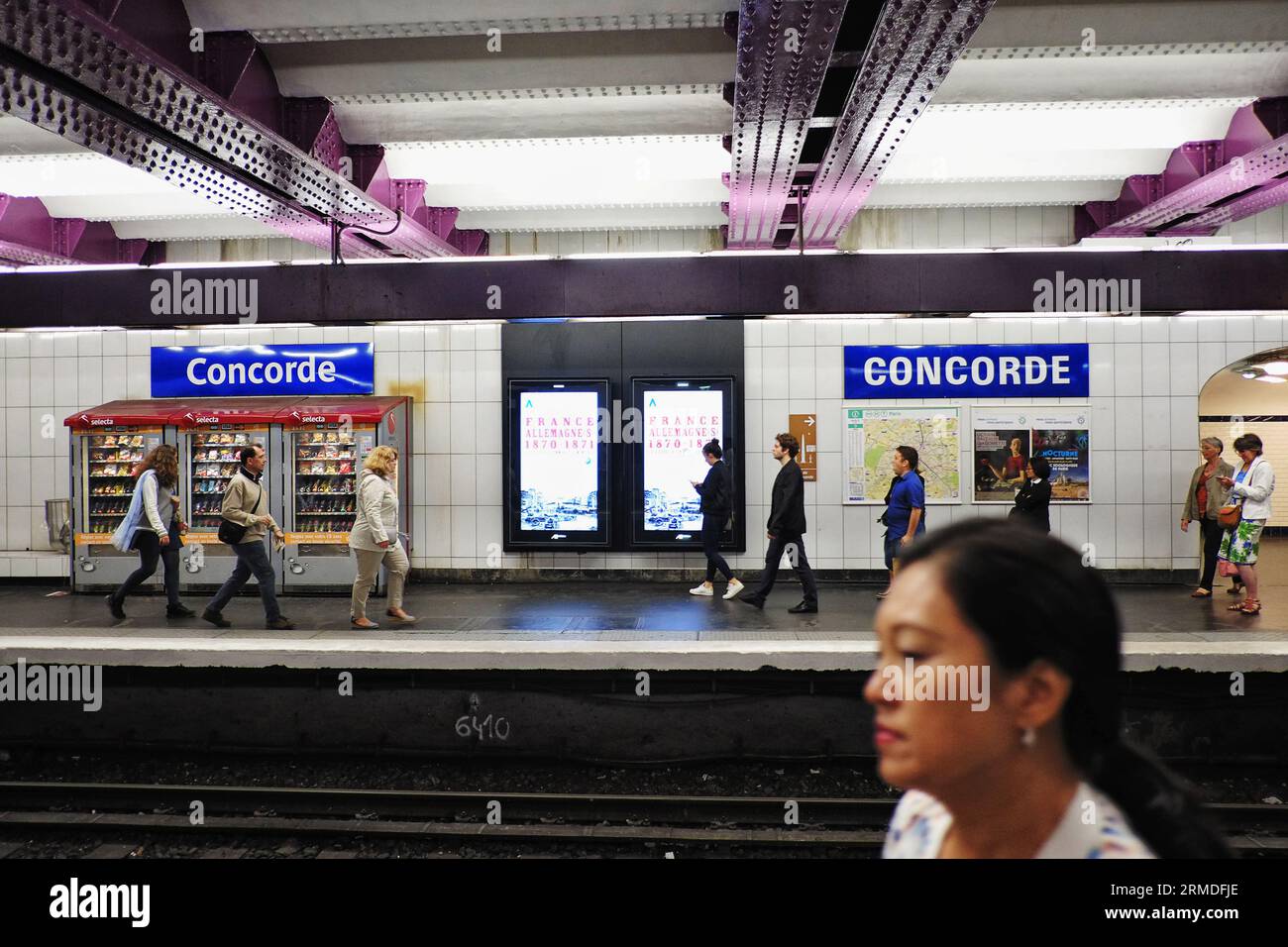 An open view of Concorde metro station platform with a few people, metro map and signs, vending machines, purple and white painted iron beams Stock Photo