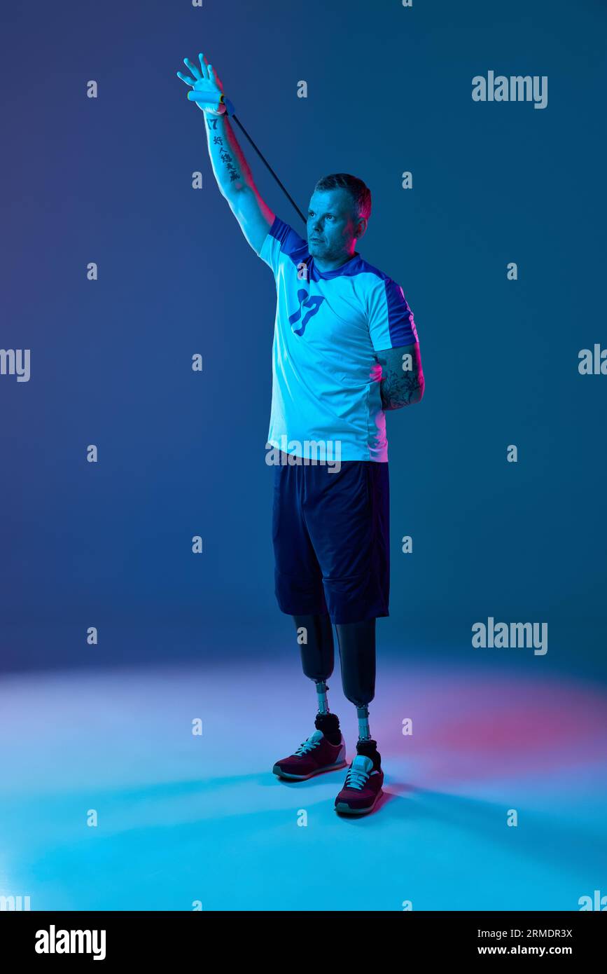 Confident man prosthetic legs doing exercises stretching hands and back with carpal expander in neon light. Motivation poster Stock Photo Alamy