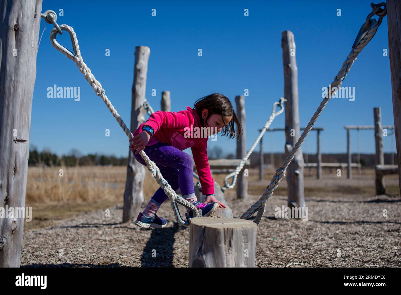 A little girl climbs onto a balance beam in an outdoor obstacle course Stock Photo