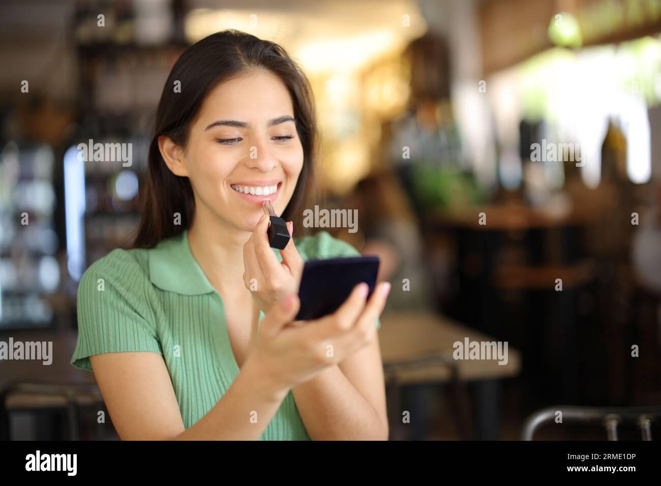 Happy woman painting lips sitting in a restaurant waiting in a date Stock Photo