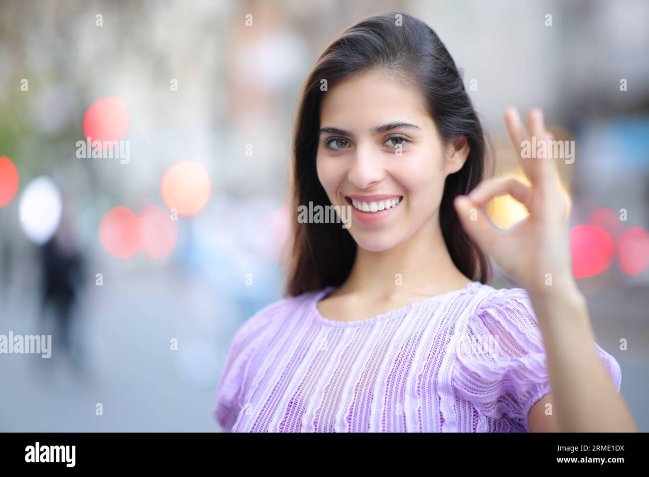 Happy woman gesturing ok standing in the street looking at you Stock Photo