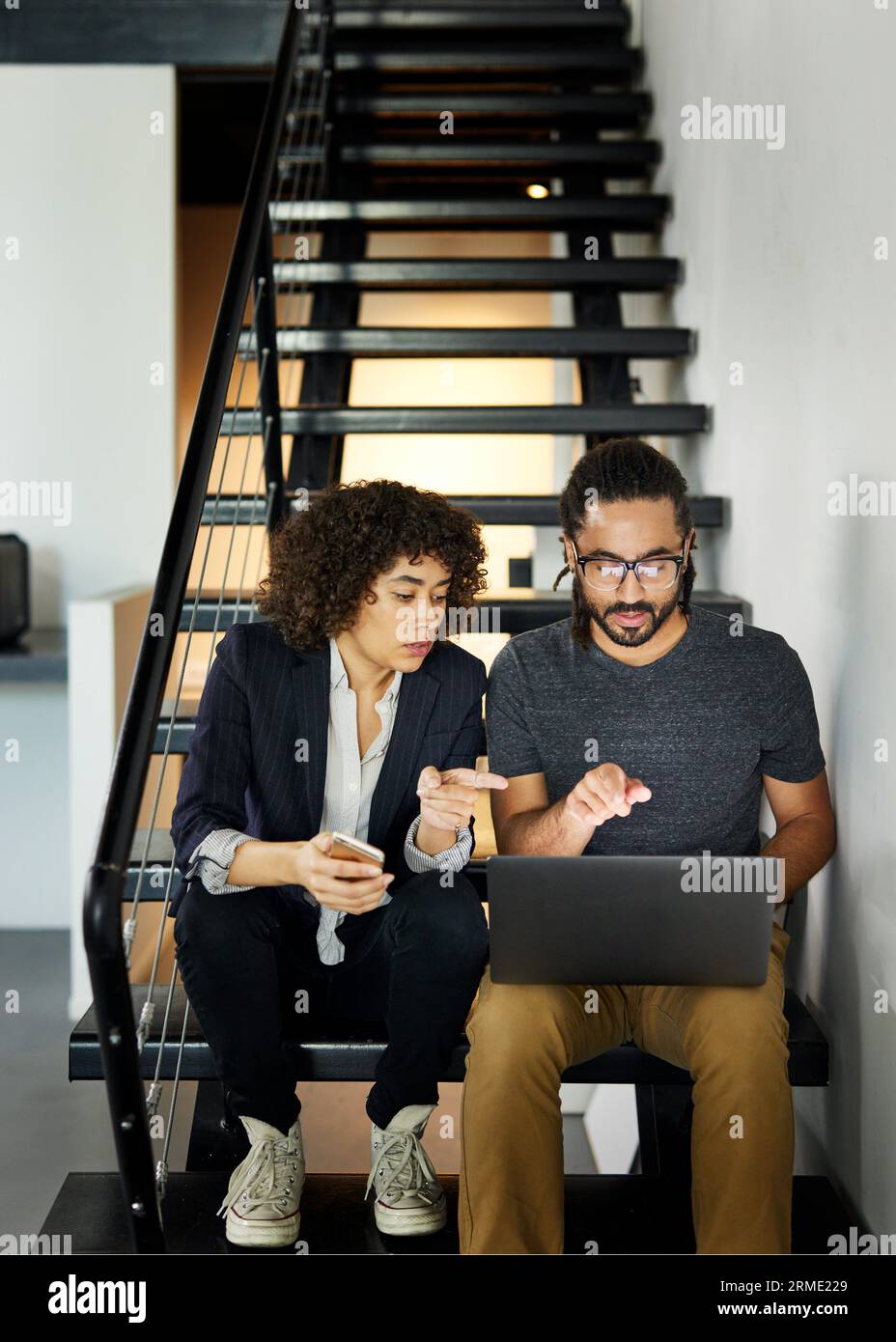 Colleagues discussing over laptop computer while sitting on steps in office Stock Photo