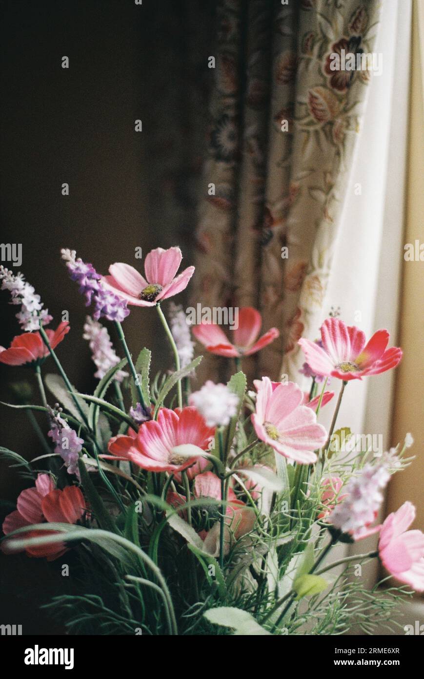 Artificial flowers in a vase by a window, home decor Stock Photo