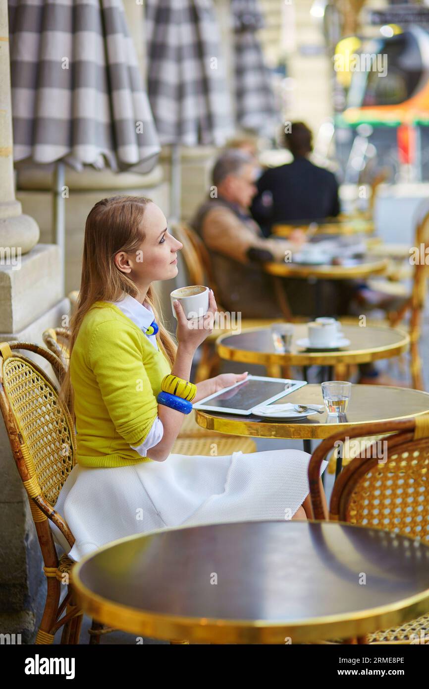 Young romantic Parisian girl drinking coffee in an outdoor cafe and using tablet Stock Photo