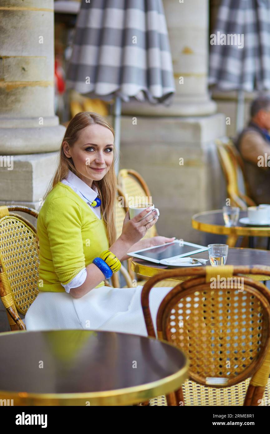 Young romantic Parisian girl drinking coffee in an outdoor cafe and using tablet Stock Photo