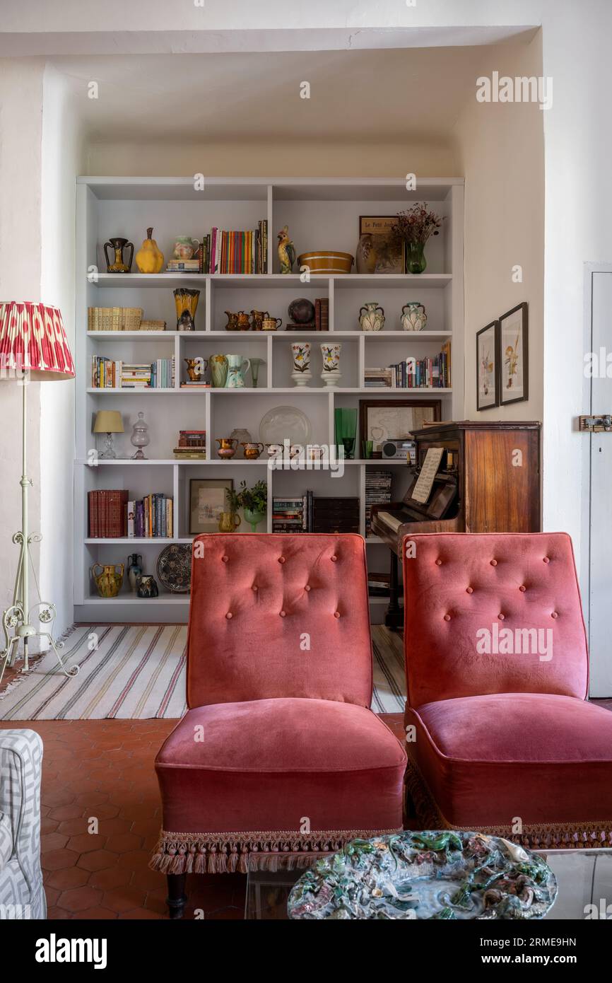 Buttoned velvet chairs from antiques fair in Belgium with curated objects on shelves in Cotignac drawing room, Var, France. Stock Photo