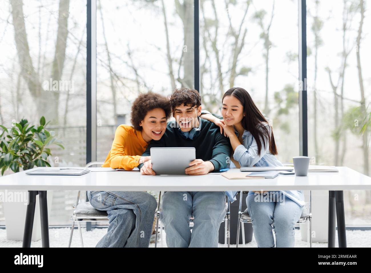 Three multiracial university students using digital tablet searching information for common project, sitting in audience Stock Photo