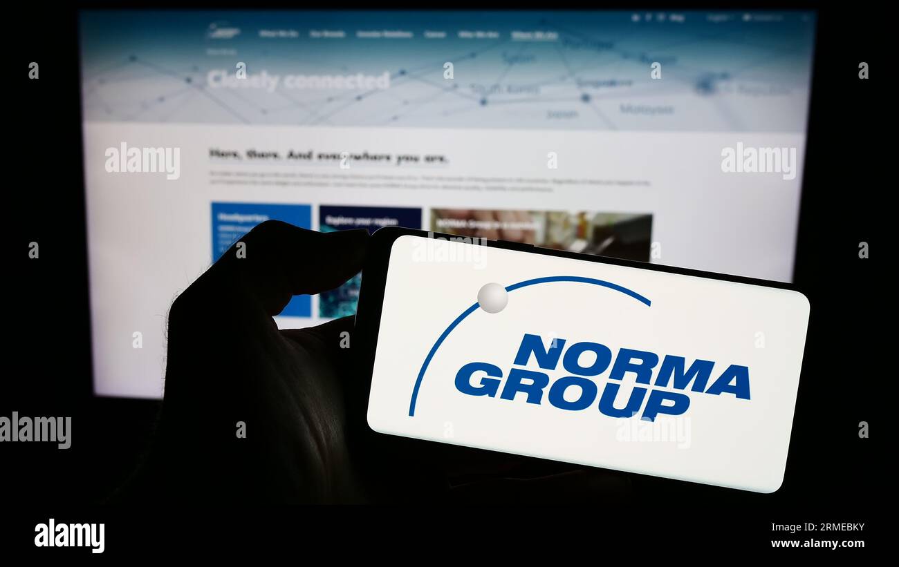 Person holding smartphone with logo of German manufacturing company Norma Group SE on screen in front of website. Focus on phone display. Stock Photo