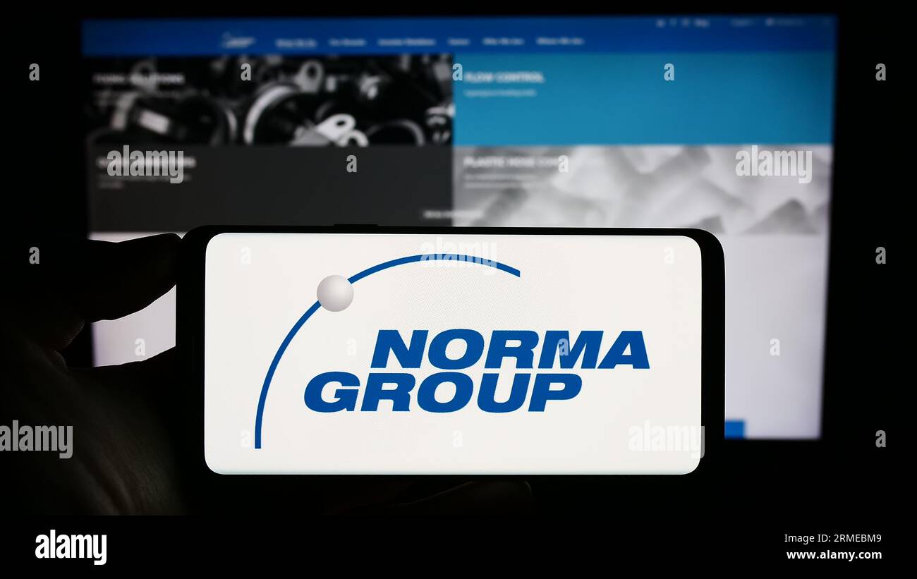Person holding cellphone with logo of German manufacturing company Norma Group SE on screen in front of business webpage. Focus on phone display. Stock Photo