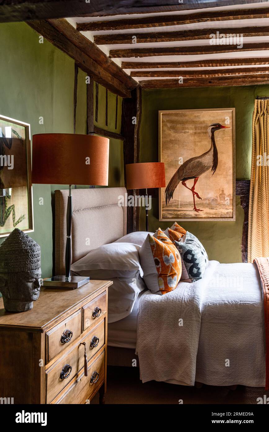 Pair of ochre lamps and print by Georges-Louis Leclerc on 'Bancha' walls in beamed bedroom of Tudor farmhouse, Surrey, UK Stock Photo