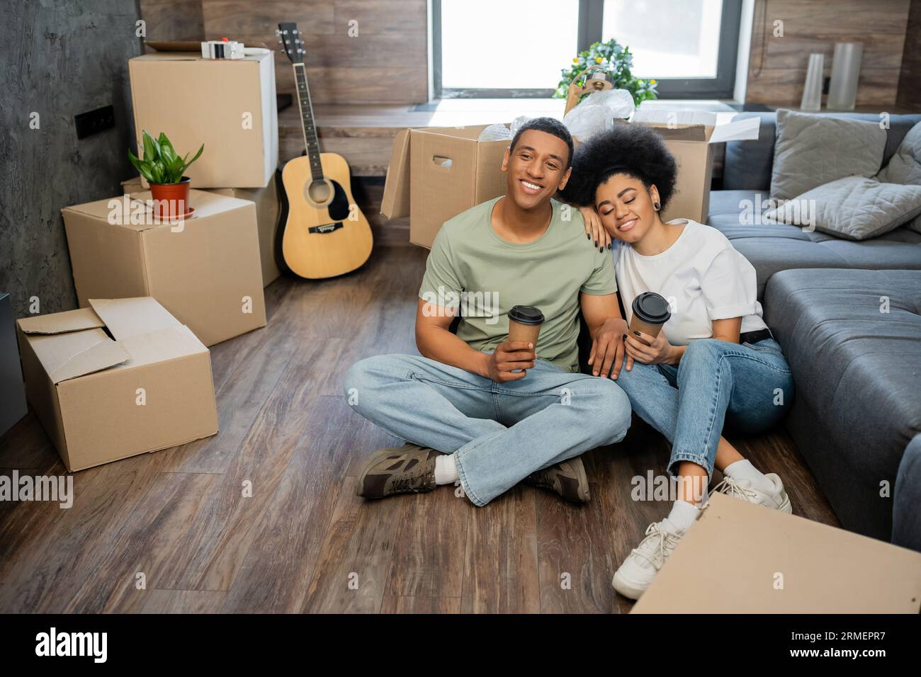 happy african american couple holding coffee while sitting near boxes ...