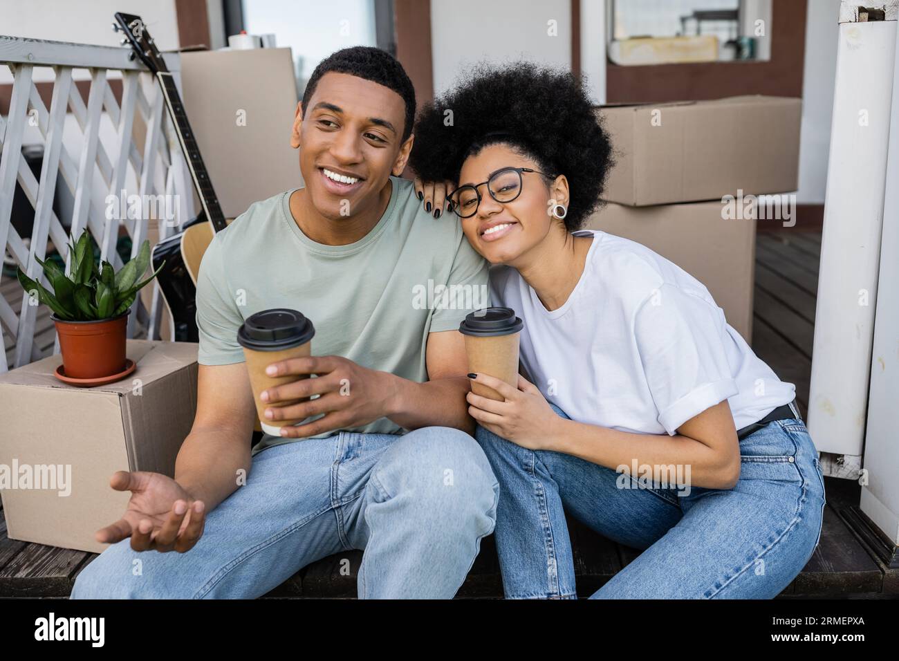 smiling african american couple with coffee to go talking near boxes on ...