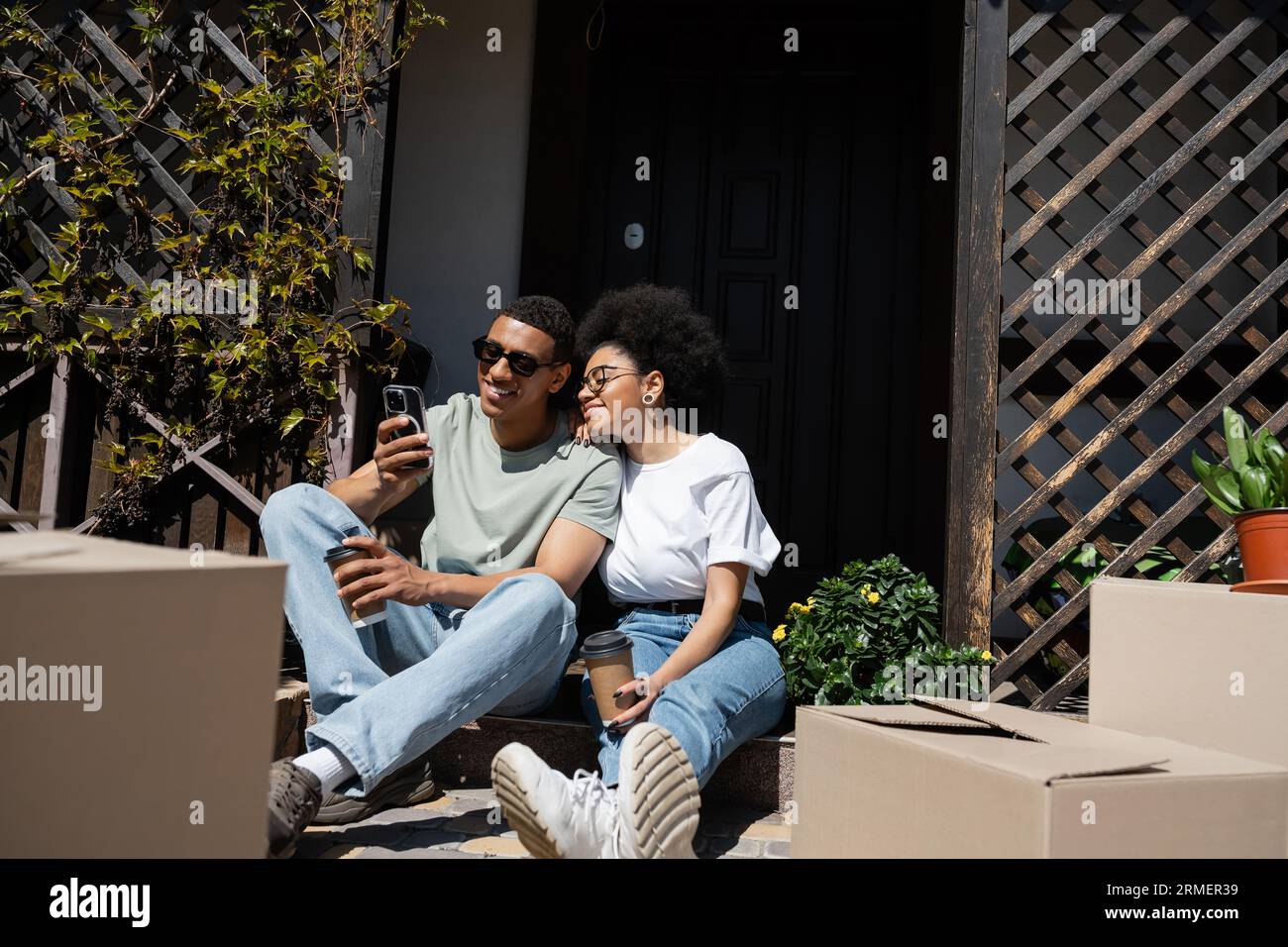 smiling african american couple with coffee to go using smartphone near ...