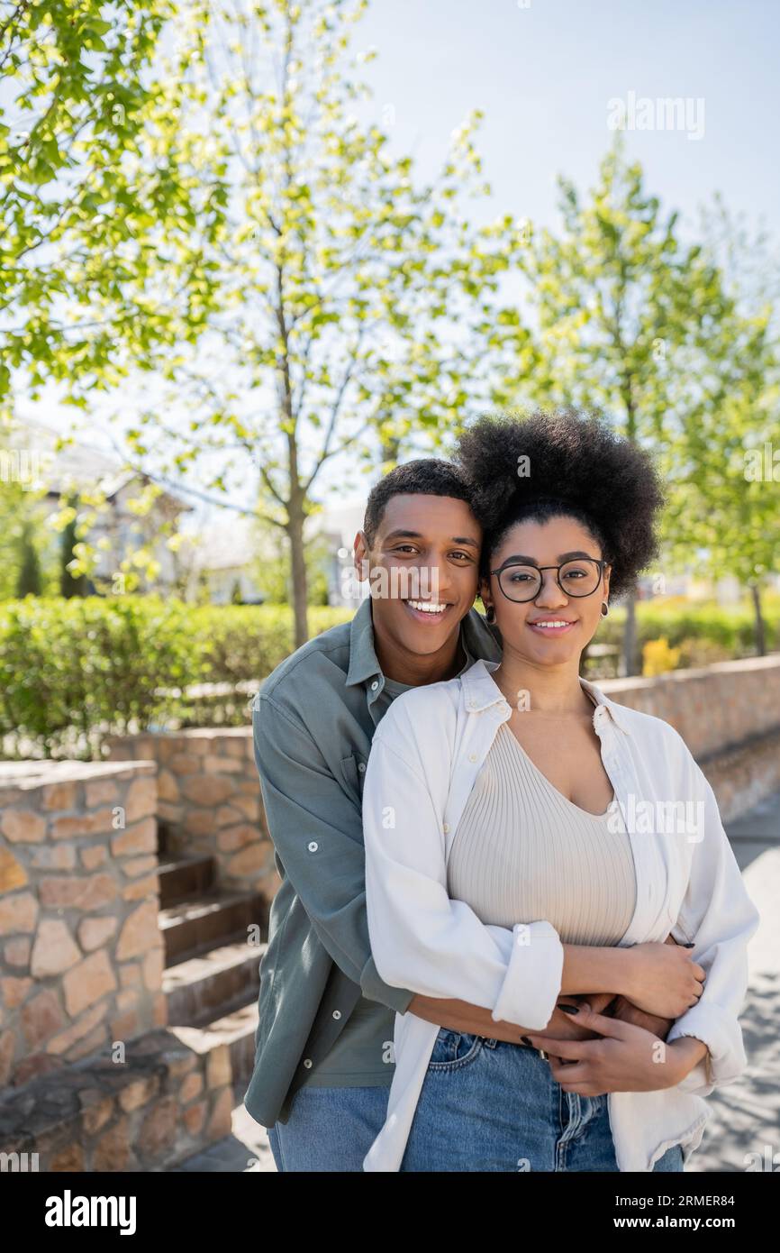 african american couple in casual clothes hugging and smiling at camera ...