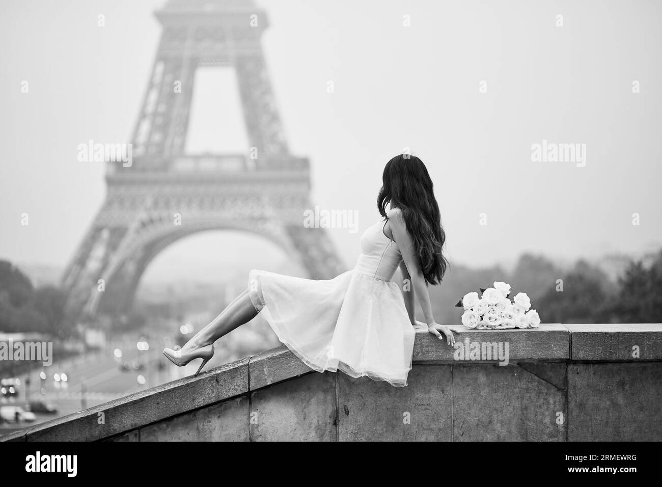 Elegant Parisian woman in pink tutu dress with white roses sitting near the Eiffel tower at Trocadero view point in Paris, France, black and white ima Stock Photo