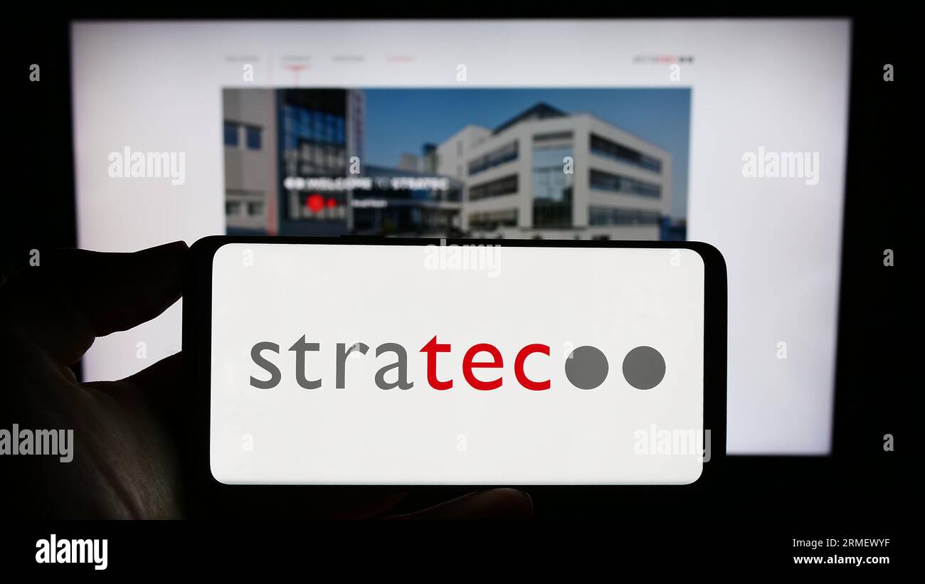 Person holding mobile phone with logo of German diagnostics company STRATEC SE on screen in front of business web page. Focus on phone display. Stock Photo