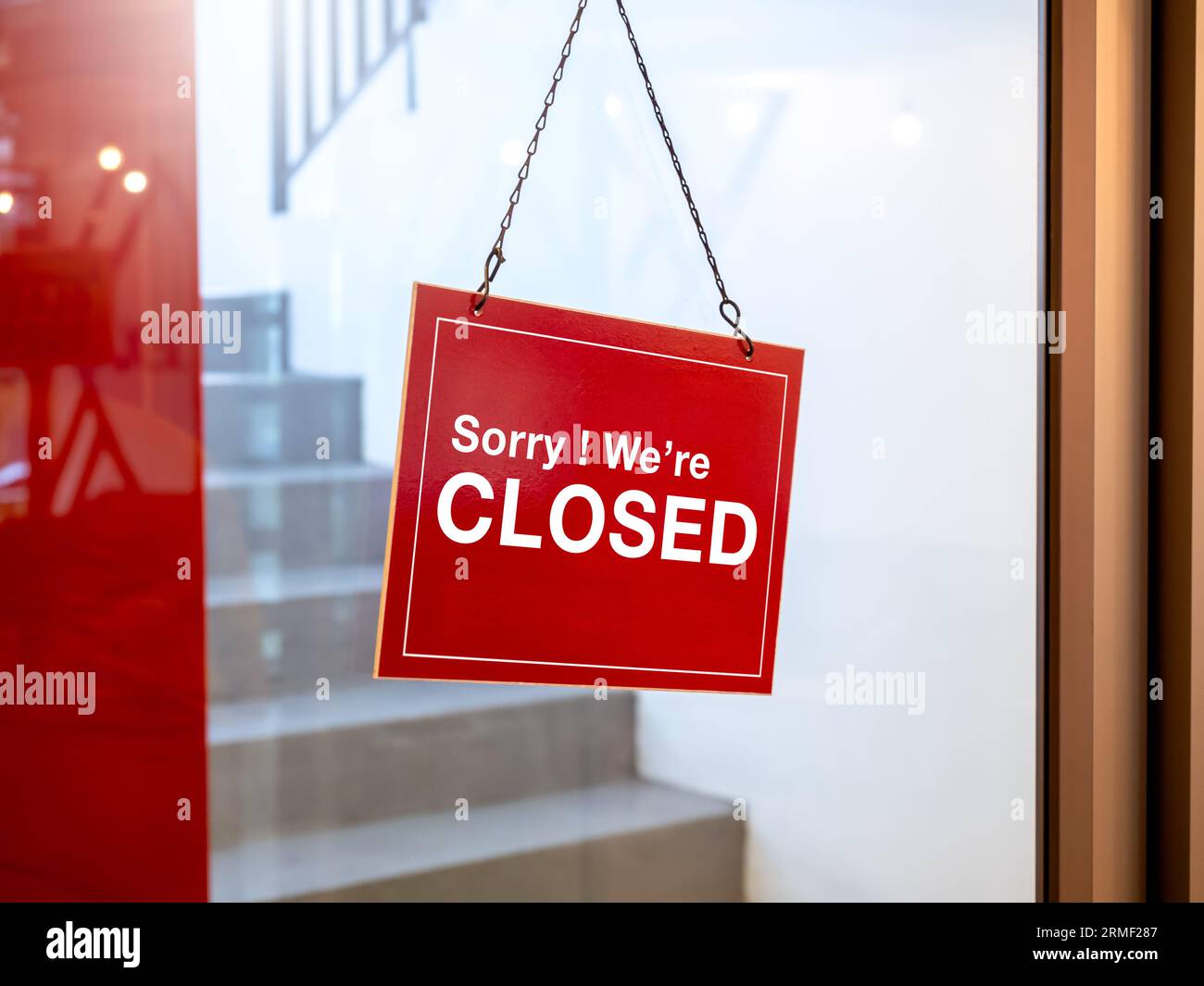 Shop closed, red and white notice sign with words 'Sorry ! we're closed' hanging on glass door in front of the staircase in the hotel or restaurant. N Stock Photo
