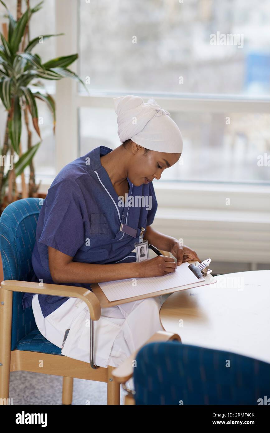 Female doctor looking sitting at table and taking notes Stock Photo