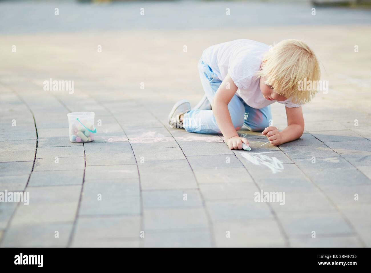 Adorable little boy drawing with colorful chalks on asphalt. Summer ...