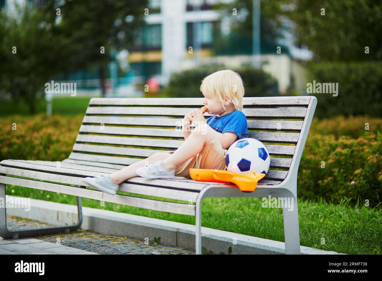 Adorable little boy sitting on the bench with lunchbox in park. Healthy