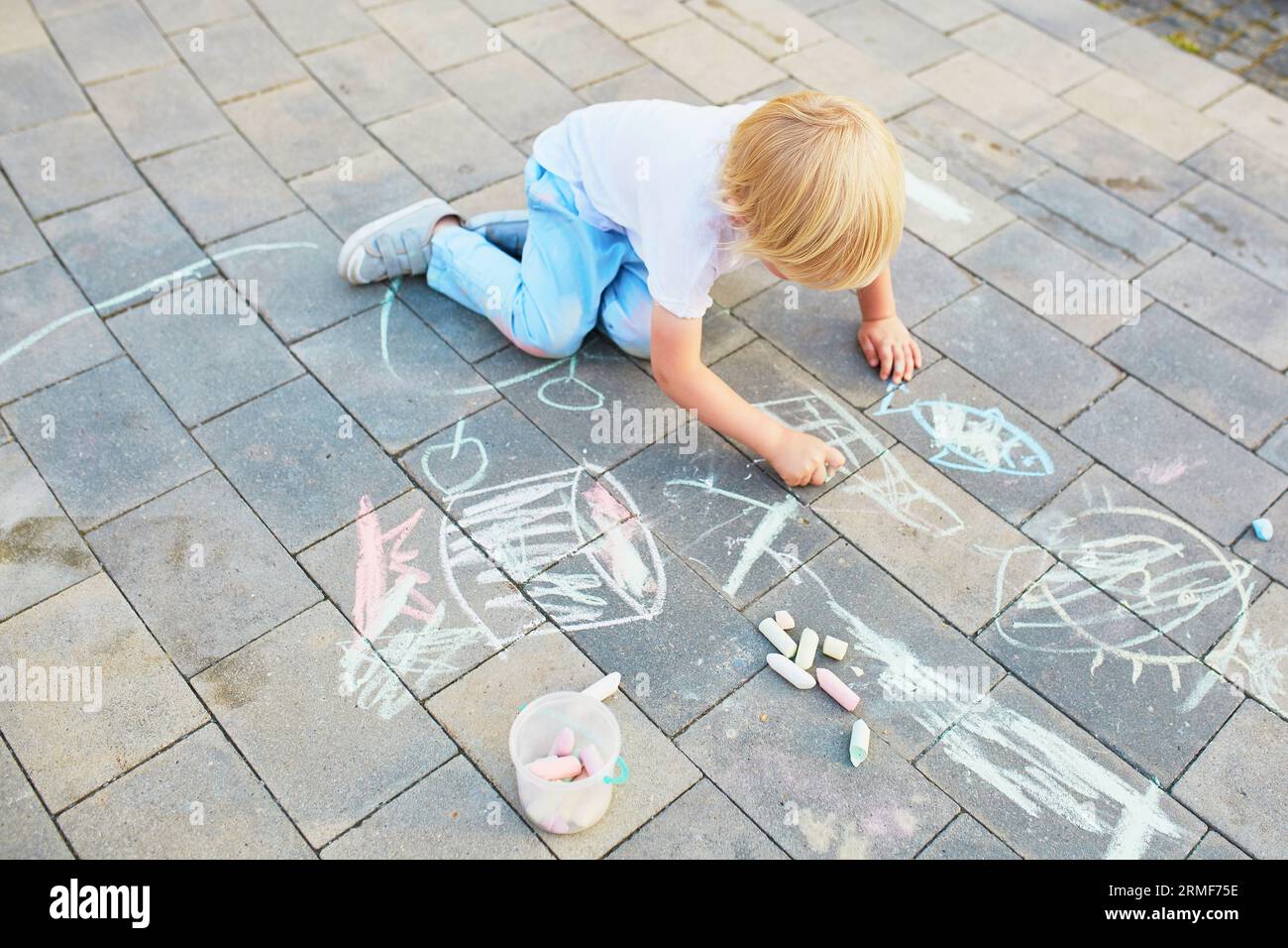 Adorable little boy drawing with colorful chalks on asphalt. Summer ...